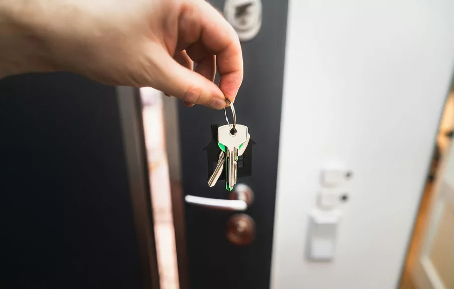 Main tenant un trousseau de clés devant une porte d’entrée ouverte, symbolisant une remise de clés ou un emménagement.